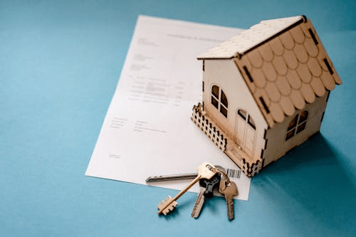 home-ownership image of a model house sitting on top of the deeds to a house and a set of keys