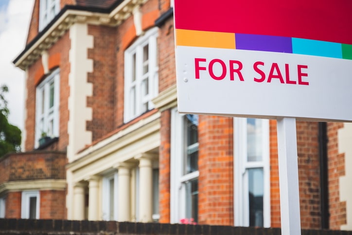 For Sale estate agent sign displayed outside a terraced house